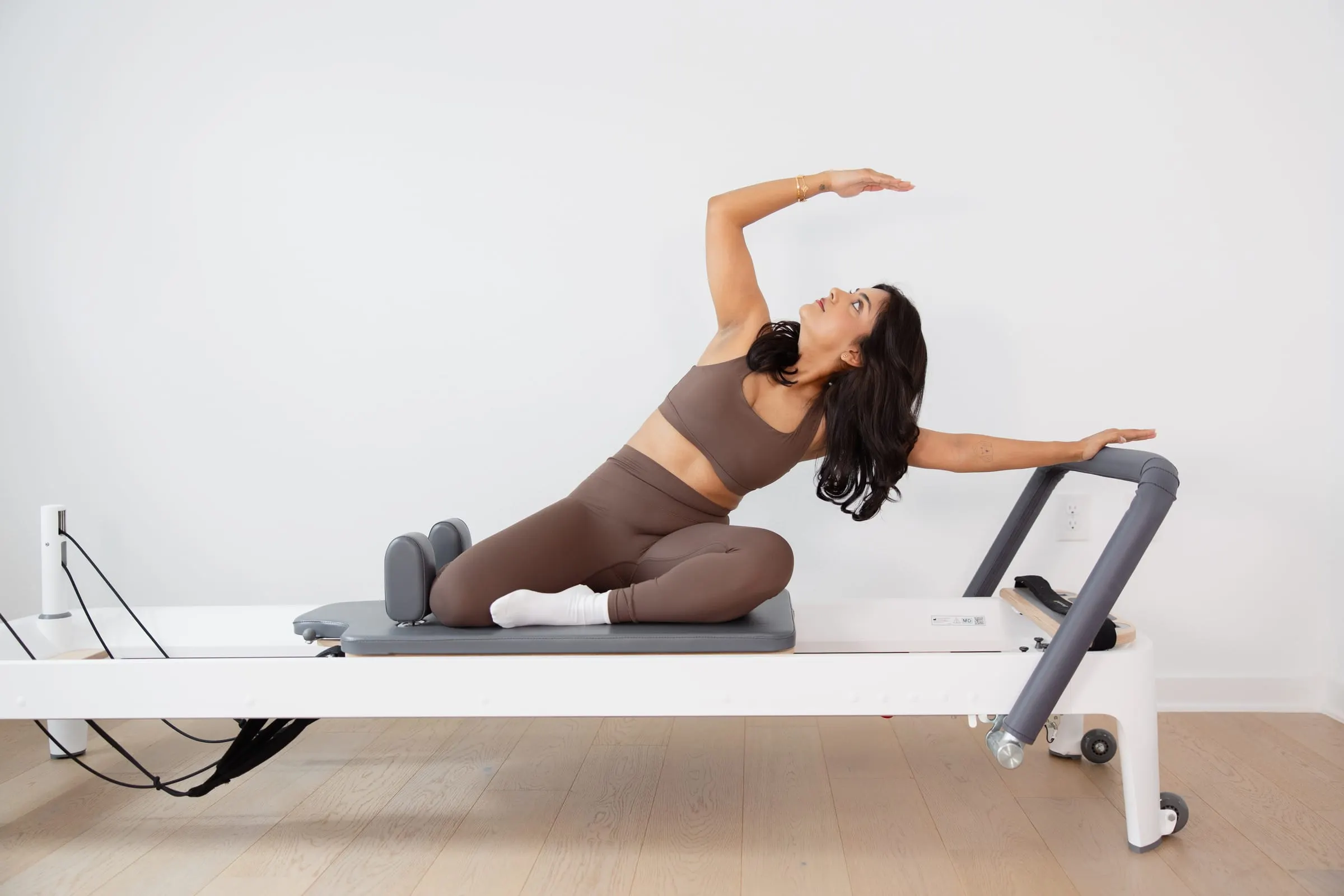 Mermaid side stretch kneeling on a reformer in a bright studio