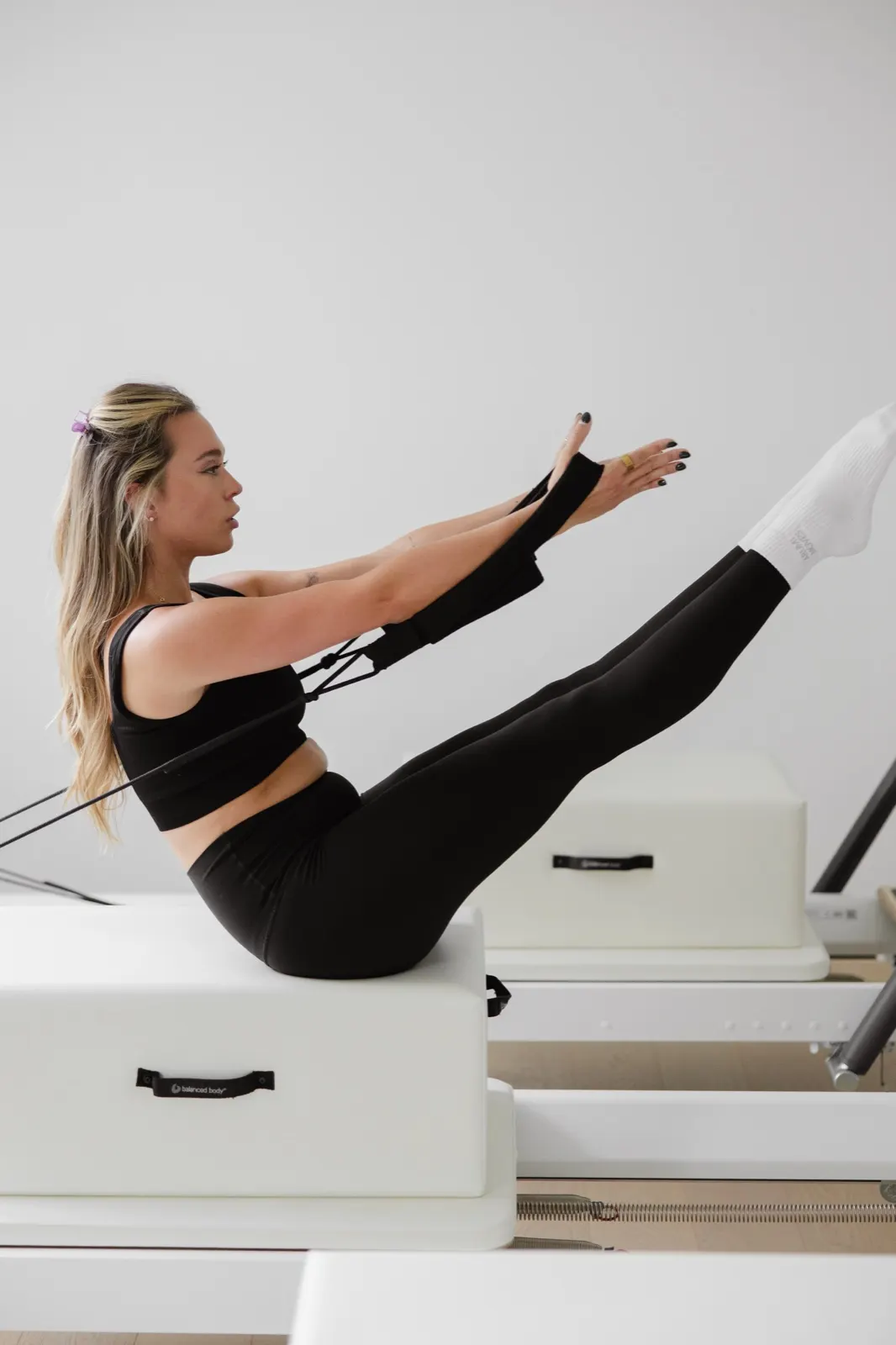 Teaser exercise seated on the reformer box holding the straps